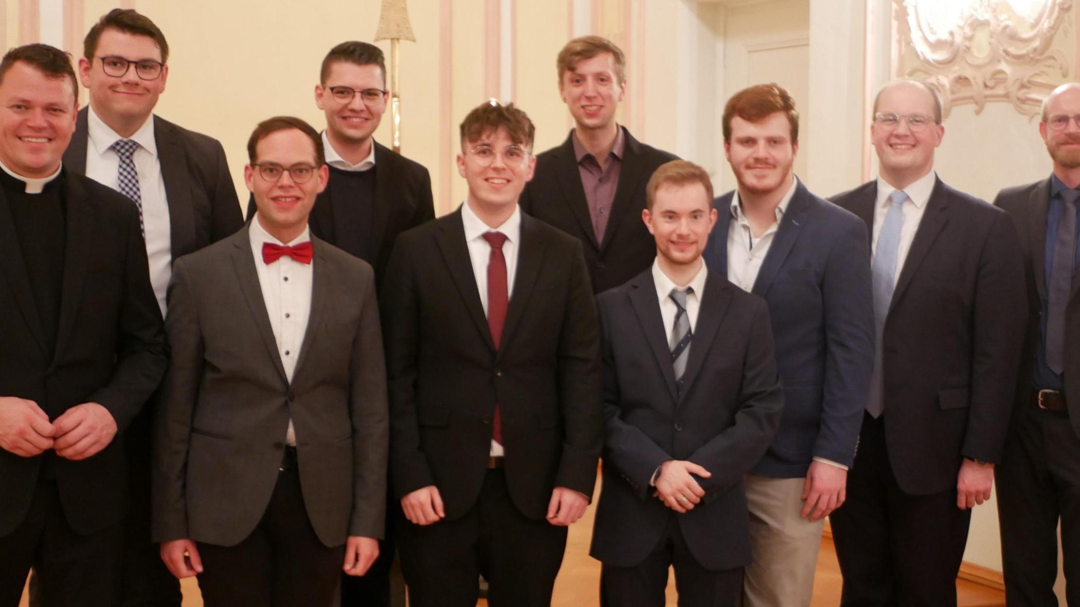 Zu sehen ist ein Gruppenfoto: Auf der Bühne der Promotionsaula stehen die Seminaristen in zwei Reihen, mit Regens Tim Sturm (links) und Spiritual Jan Lehmann (rechts). Alle tragen einen Anzug und sind festlich gekleidet.