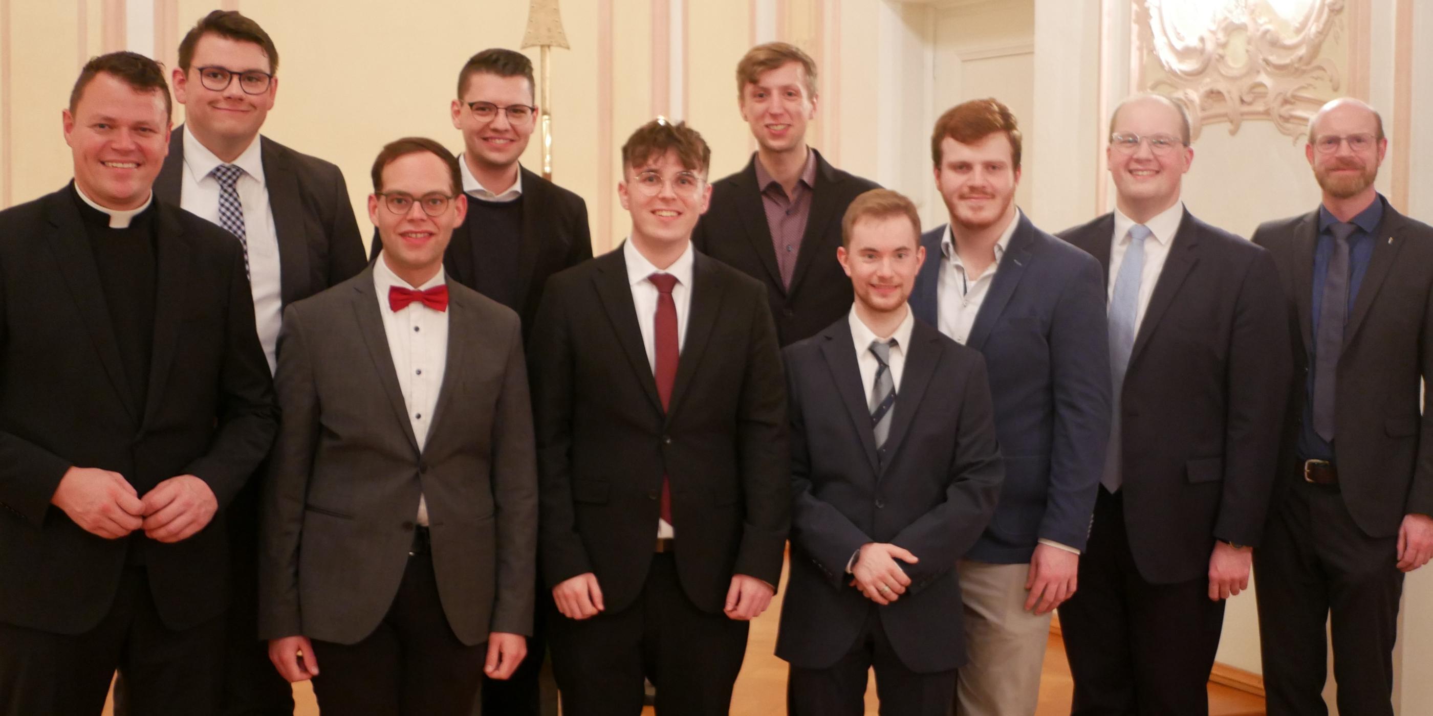 Zu sehen ist ein Gruppenfoto: Auf der Bühne der Promotionsaula stehen die Seminaristen in zwei Reihen, mit Regens Tim Sturm (links) und Spiritual Jan Lehmann (rechts). Alle tragen einen Anzug und sind festlich gekleidet.