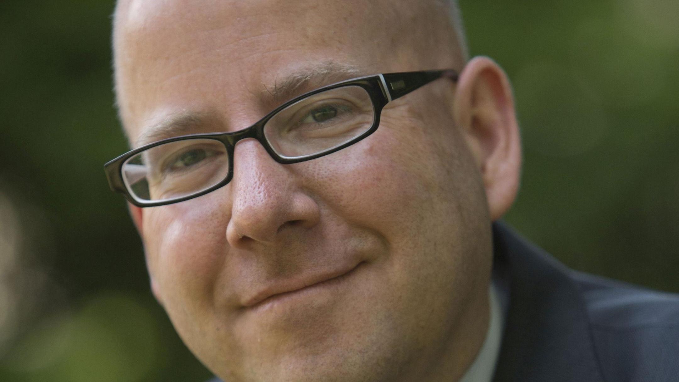 Portraitfoto von Oliver Laufer-Schmitt vor einem grünen, unscharfen Hintergrund.