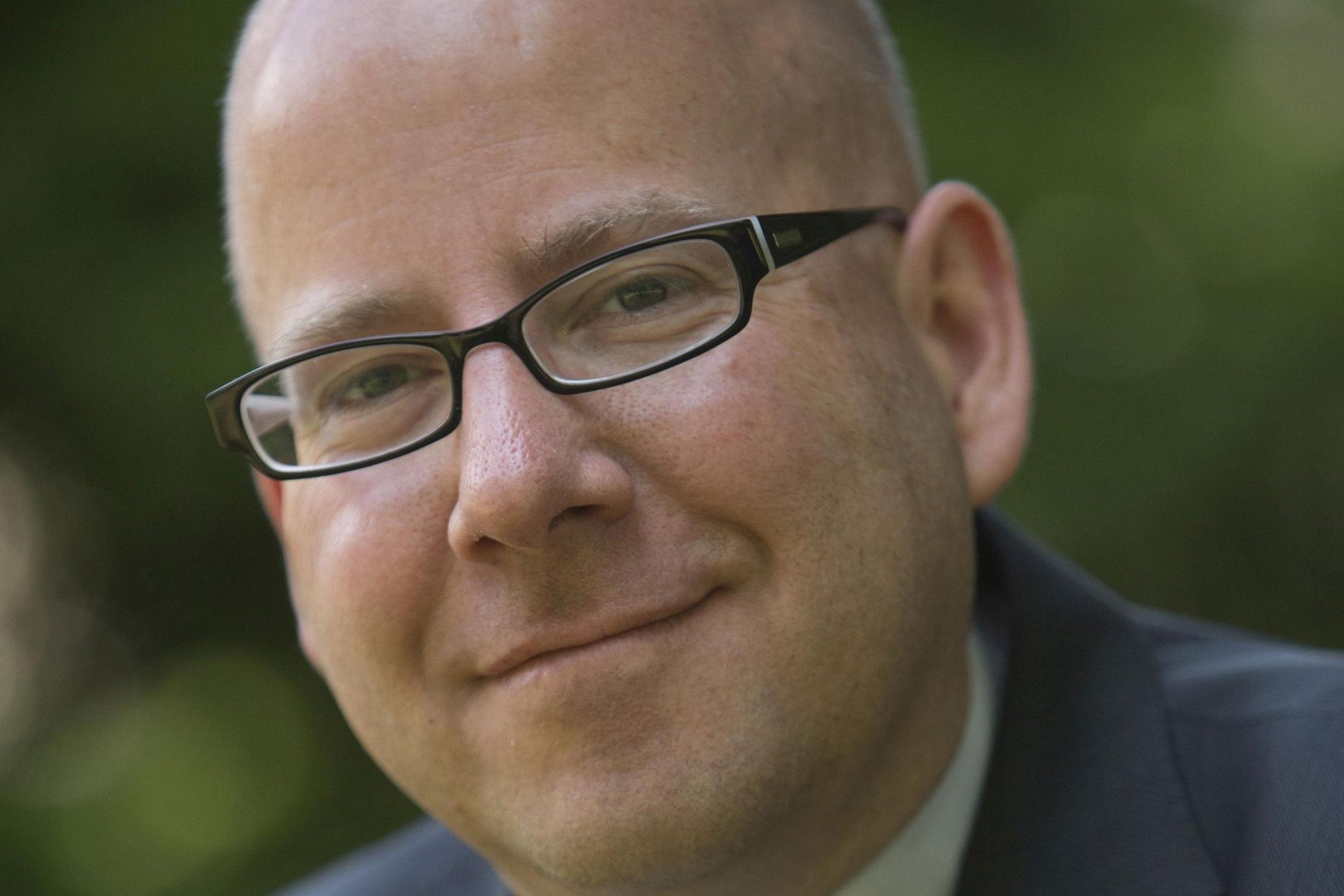 Portraitfoto von Oliver Laufer-Schmitt vor einem grünen, unscharfen Hintergrund.