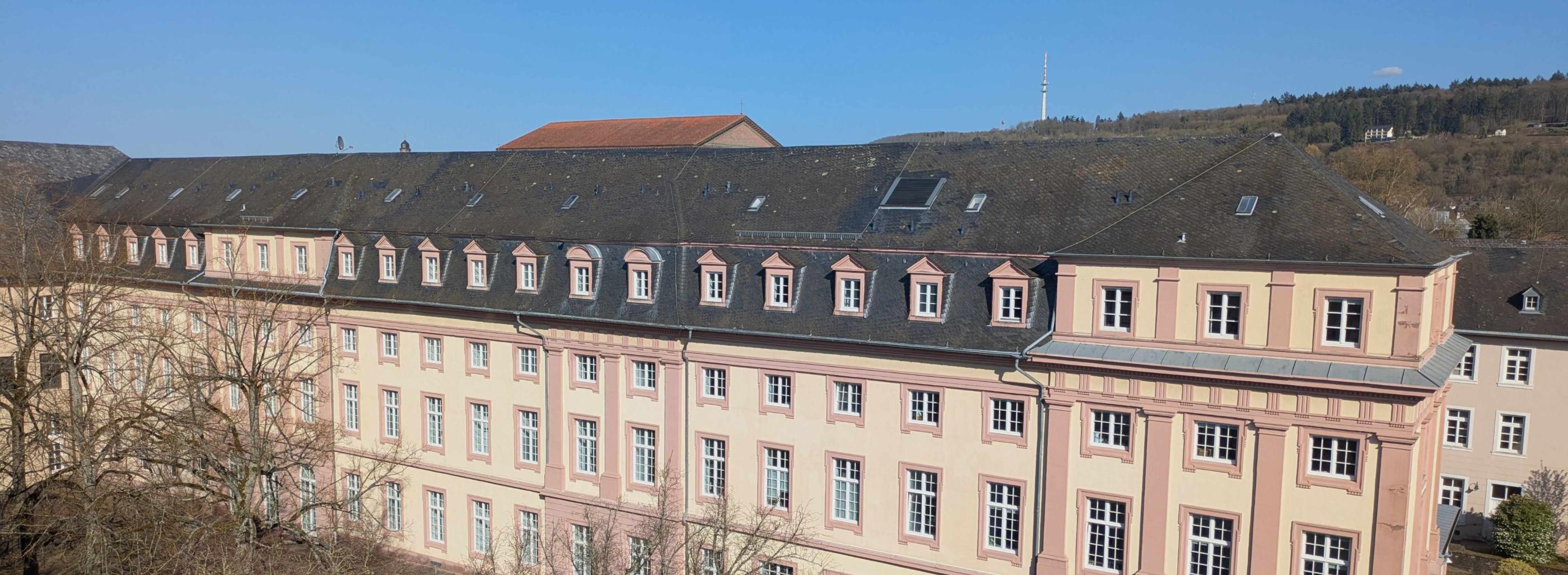 Man sieht das Clementinum, das Hauptgebäude des Priesterseminars. Im Vordergrund sind einige Bäume ohne Laub. Im Hintergrund ein blauer Himmel.