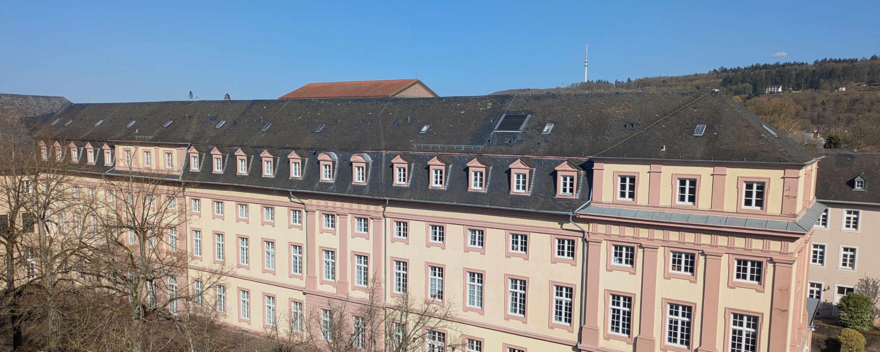 Man sieht das Clementinum, das Hauptgebäude des Priesterseminars. Im Vordergrund sind einige Bäume ohne Laub. Im Hintergrund ein blauer Himmel.