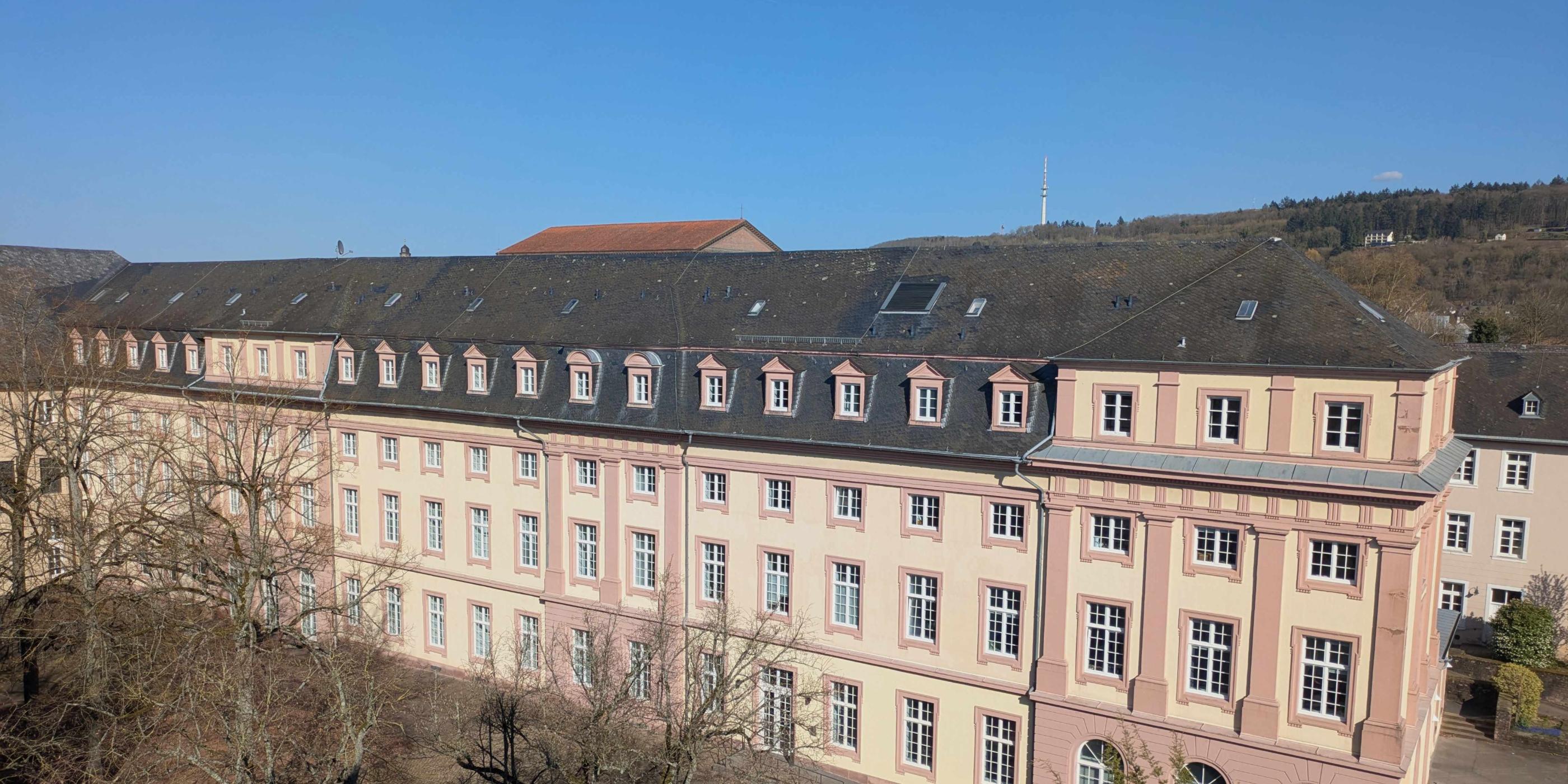 Man sieht das Clementinum, das Hauptgebäude des Priesterseminars. Im Vordergrund sind einige Bäume ohne Laub. Im Hintergrund ein blauer Himmel.