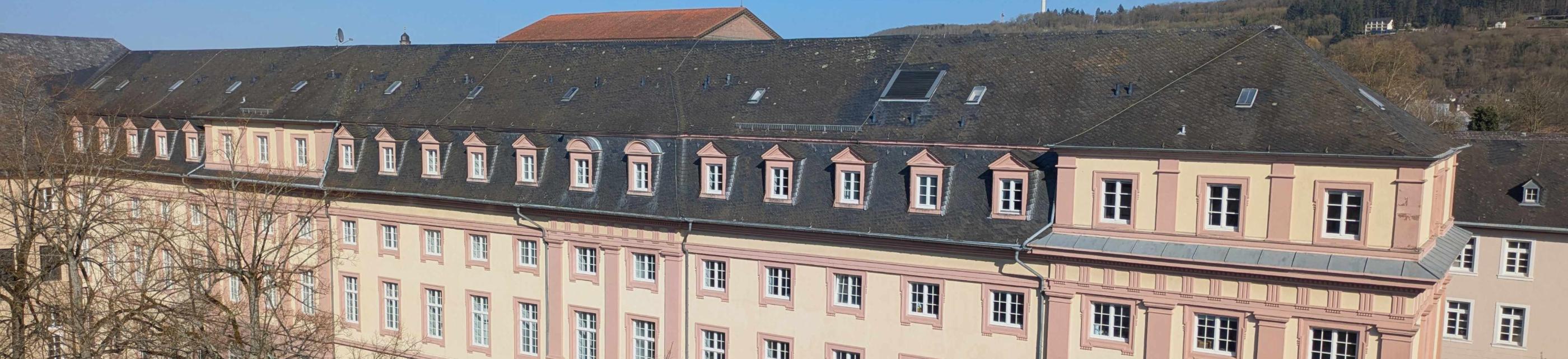 Man sieht das Clementinum, das Hauptgebäude des Priesterseminars. Im Vordergrund sind einige Bäume ohne Laub. Im Hintergrund ein blauer Himmel.