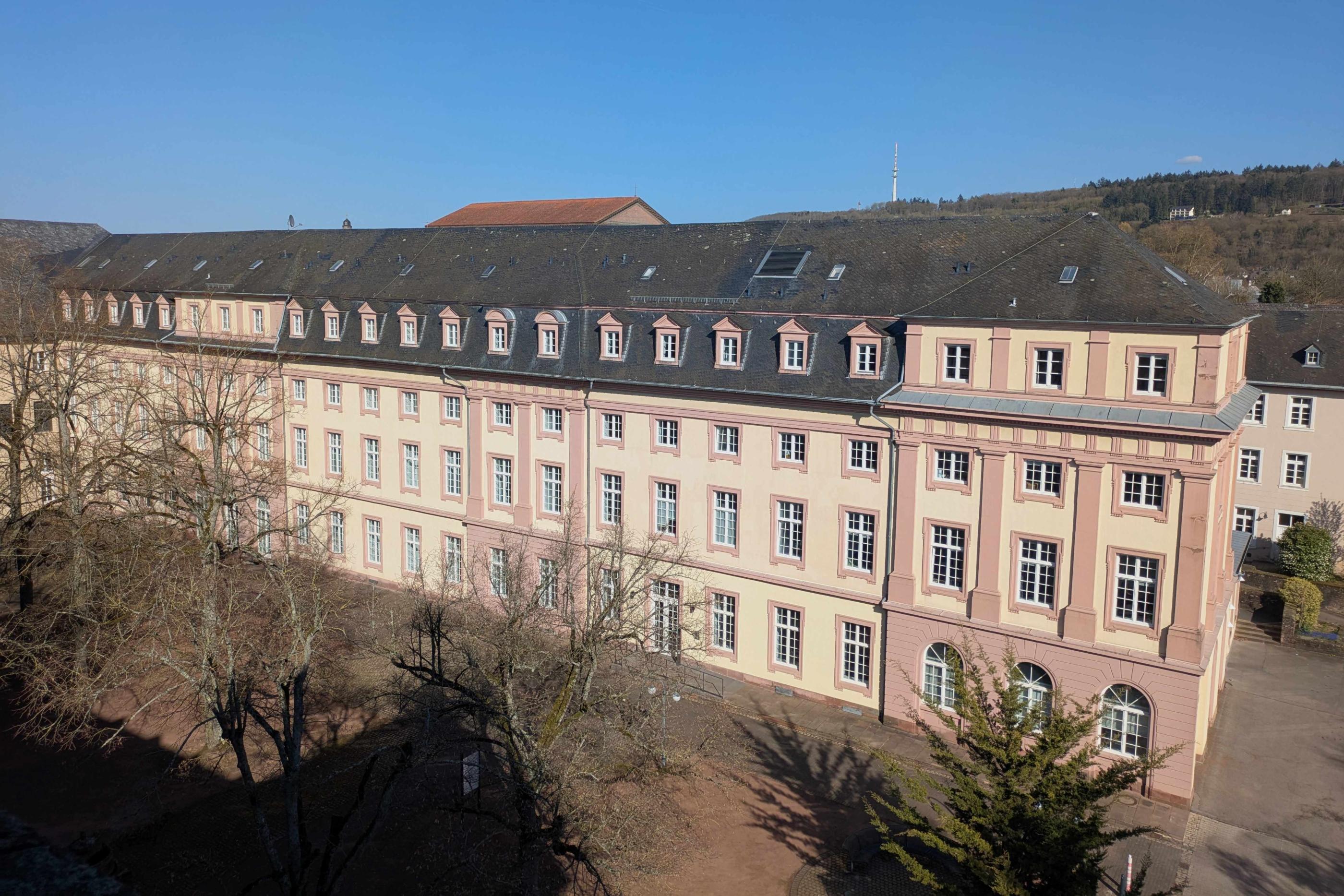 Man sieht das Clementinum, das Hauptgebäude des Priesterseminars. Im Vordergrund sind einige Bäume ohne Laub. Im Hintergrund ein blauer Himmel.