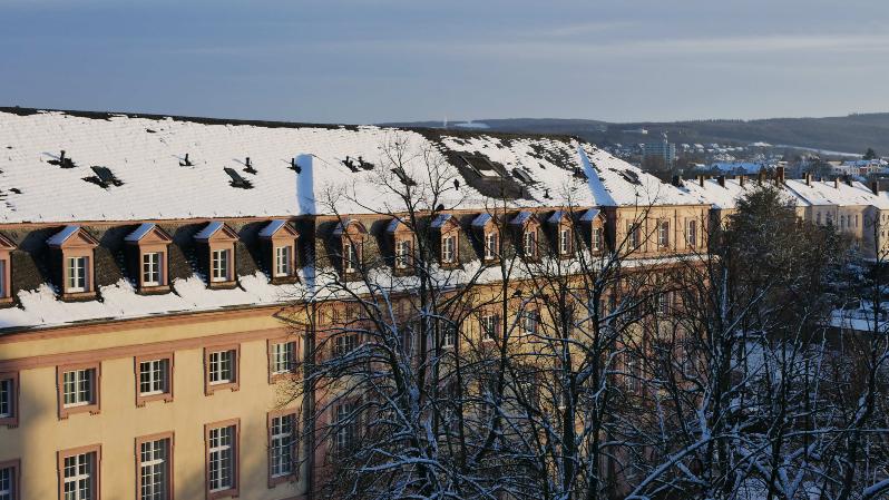 Man sieht das Clementinum, das Hauptgebäude des Priesterseminars, bedeckt von Schnee. Im Vordergrund sind einige Bäume ohne Laub. Im Hintergrund ein leicht bewölkter blauer Himmel.