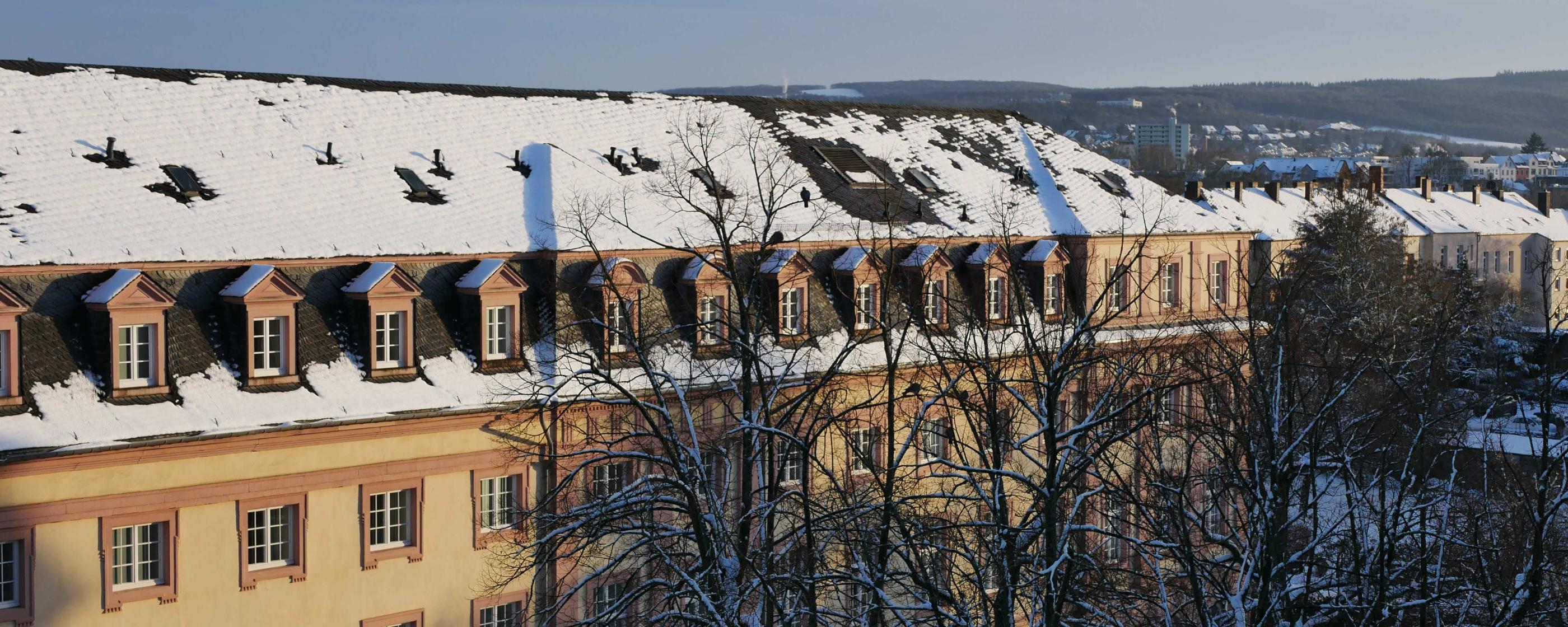 Man sieht das Clementinum, das Hauptgebäude des Priesterseminars, bedeckt von Schnee. Im Vordergrund sind einige Bäume ohne Laub. Im Hintergrund ein leicht bewölkter blauer Himmel.