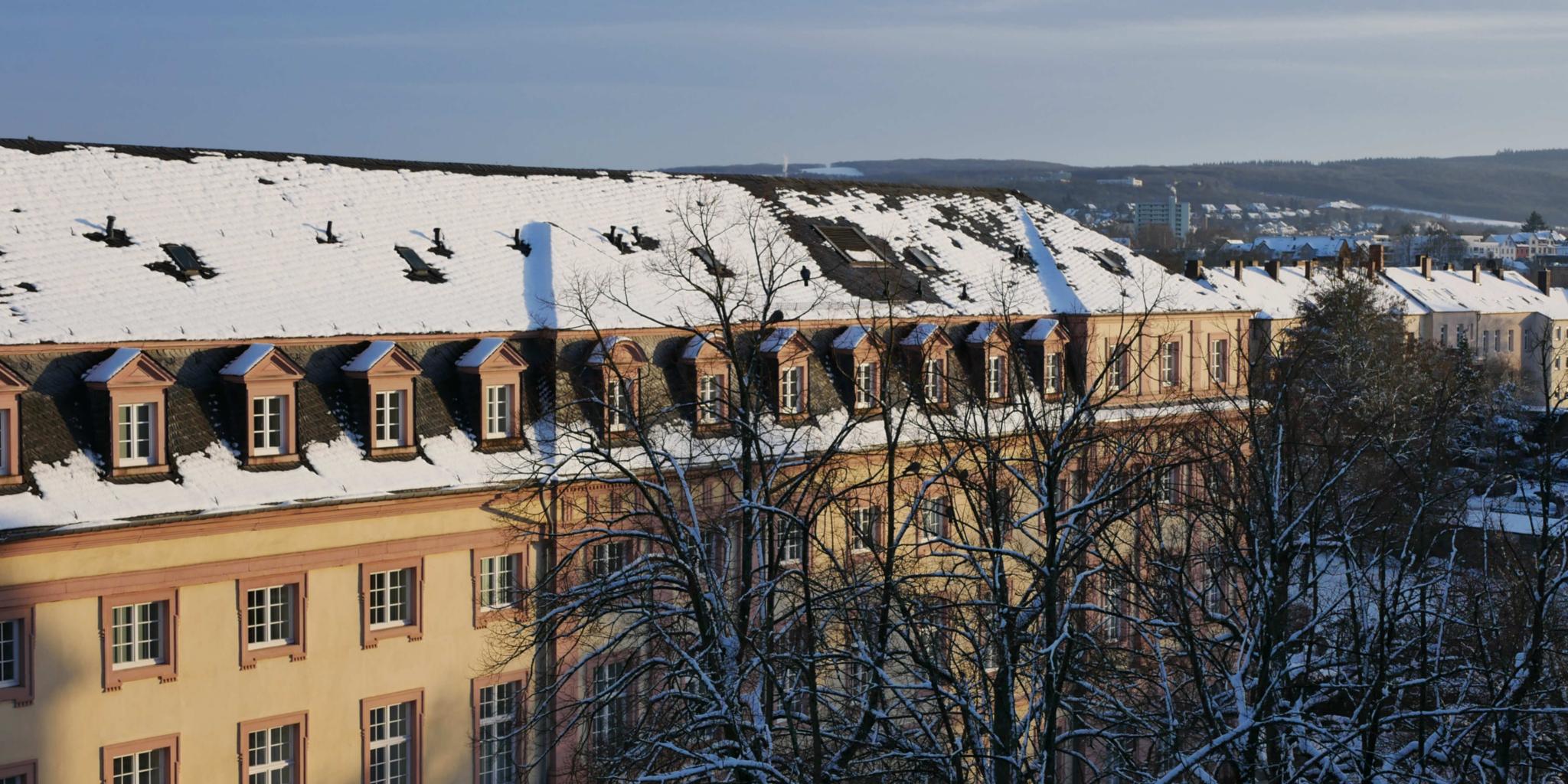 Man sieht das Clementinum, das Hauptgebäude des Priesterseminars, bedeckt von Schnee. Im Vordergrund sind einige Bäume ohne Laub. Im Hintergrund ein leicht bewölkter blauer Himmel.