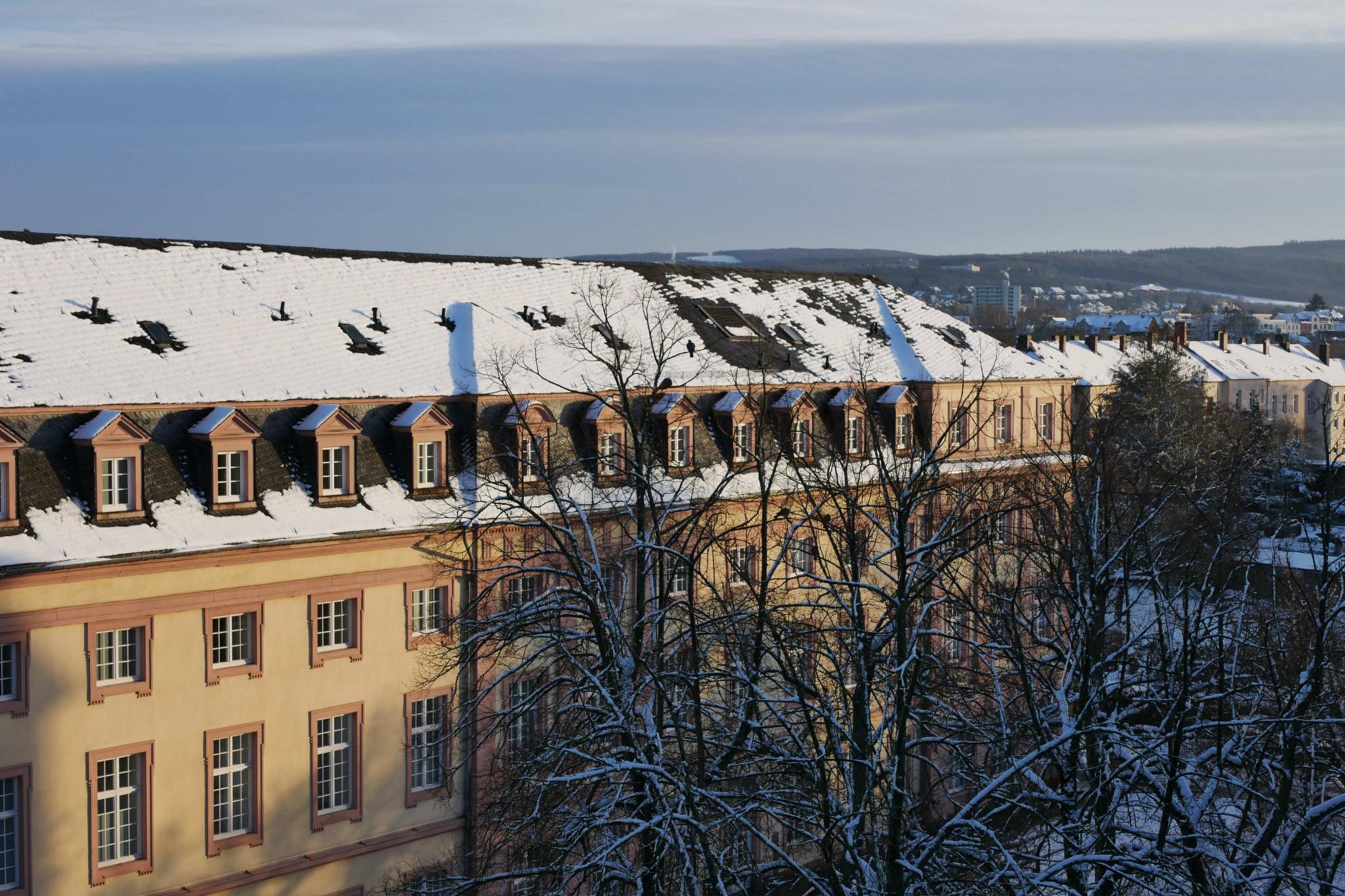 Man sieht das Clementinum, das Hauptgebäude des Priesterseminars, bedeckt von Schnee. Im Vordergrund sind einige Bäume ohne Laub. Im Hintergrund ein leicht bewölkter blauer Himmel.