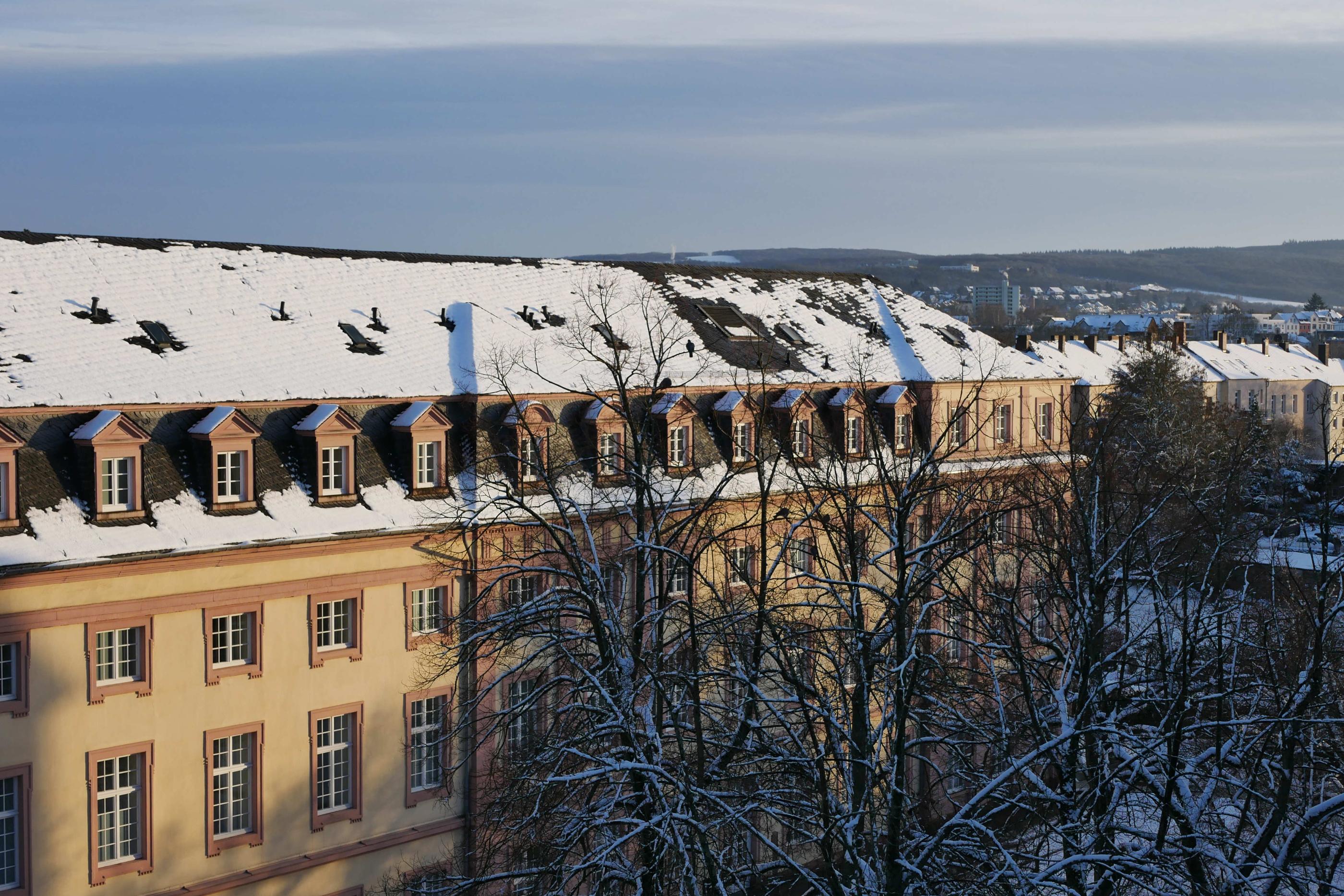 Man sieht das Clementinum, das Hauptgebäude des Priesterseminars, bedeckt von Schnee. Im Vordergrund sind einige Bäume ohne Laub. Im Hintergrund ein leicht bewölkter blauer Himmel.