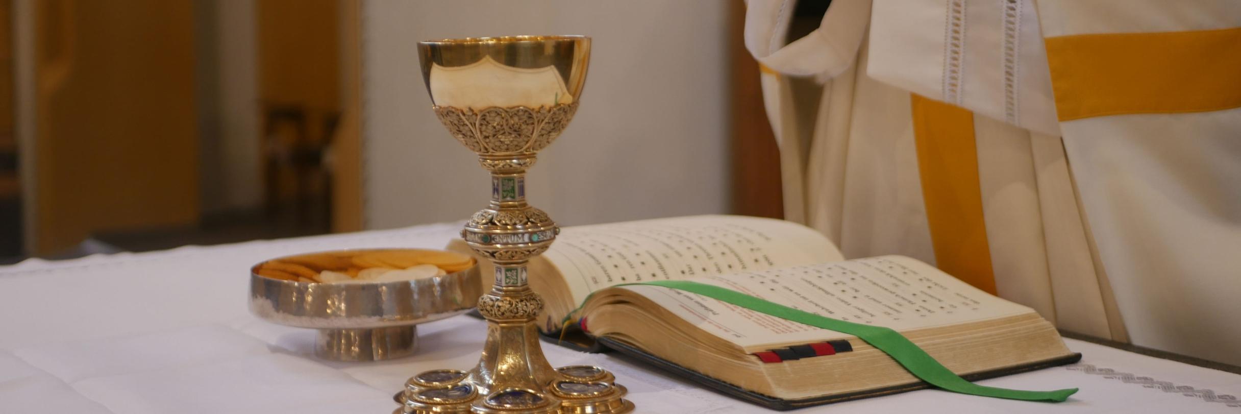 Man sieht einen Altar. Darauf befinden sich ein Messbuch, ein goldener Kelch und eine mit Hostien gefüllte silberne Schale