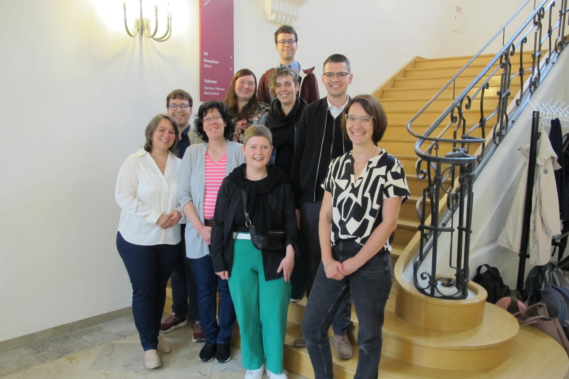 Neun lachende Menschen stehen auf eine Treppe.